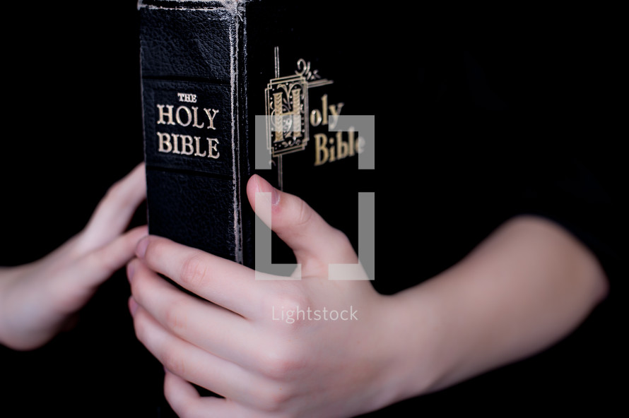 Child's hands holding a closed Bible.