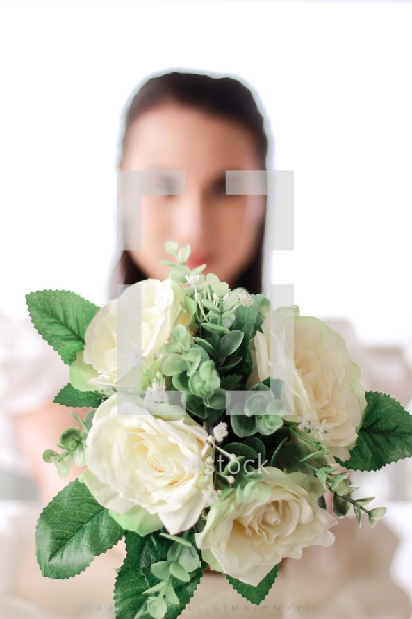 a bride holding out a bouquet of white roses 