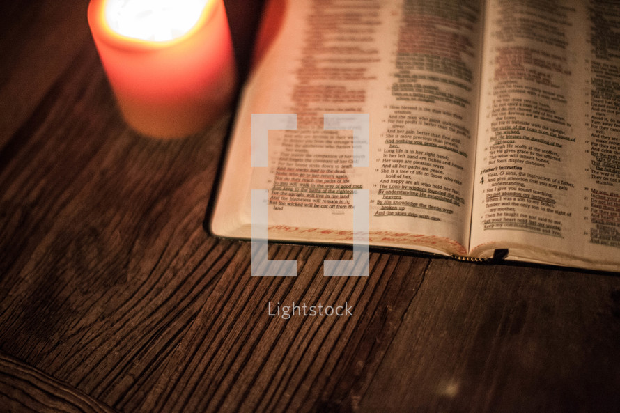 open Bible on a table and a glowing candle
