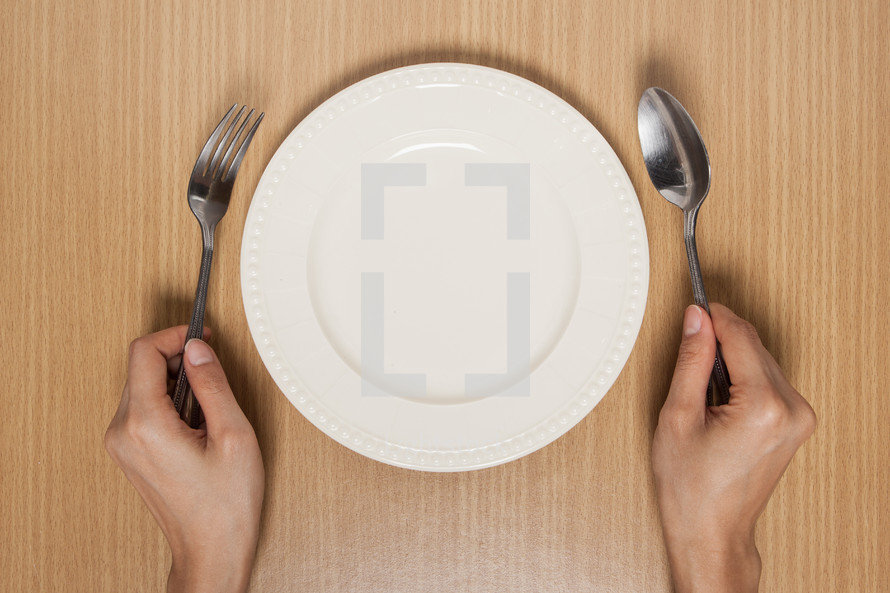 hands holding silverware beside an empty plate 