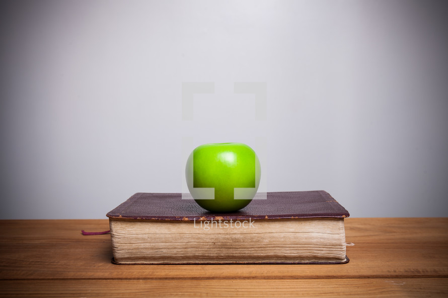 a green apple on a book on a desk 