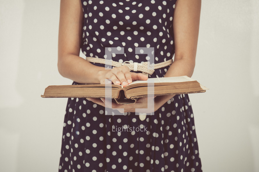 torso of a woman in a polka dot dress reading a Bible 