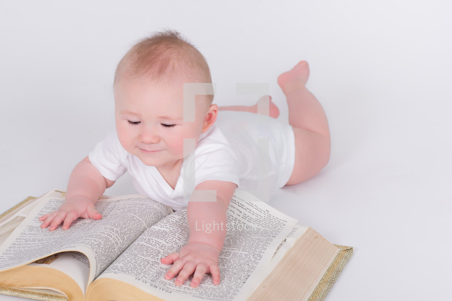 Infant laying on the floor, hands stretched out on a giant bible
