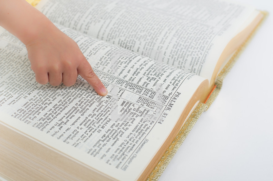 Child's hand pointing to a scripture in a open bible