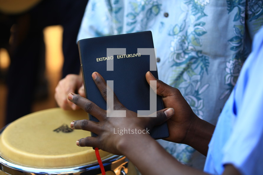 Hands holding Bible with musician in background.