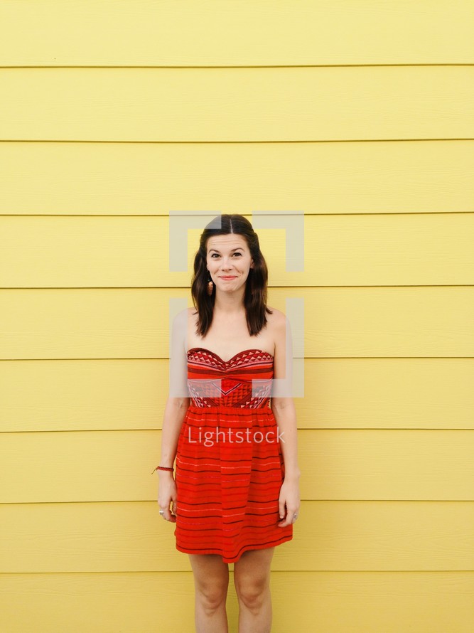 woman standing in a red dress against a yellow wall 