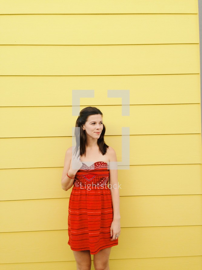 woman in a red dress standing against a yellow wall 