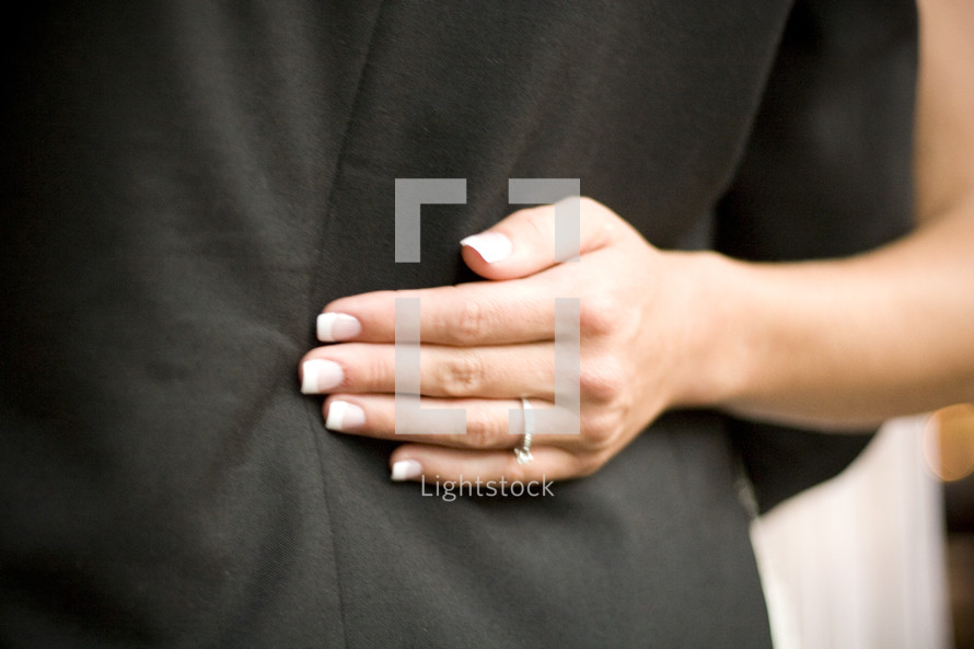 Woman's hand resting on back of man's jacket.