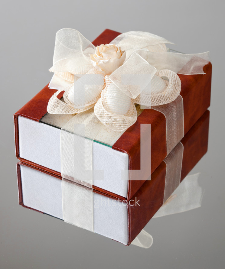 gift box with a brown cover is wrapped up by a beige tape with a bow