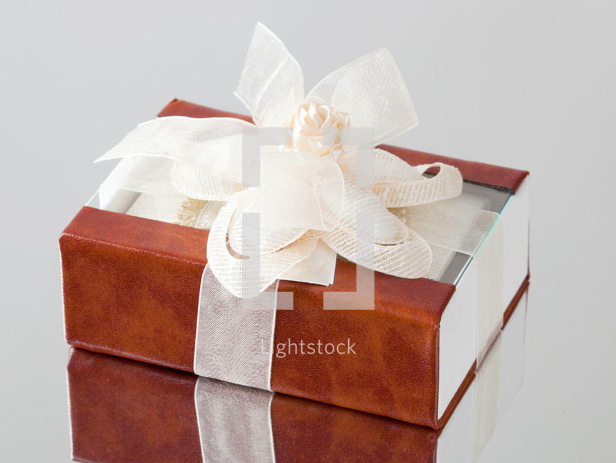 The gift box with a brown cover is wrapped up by a beige tape with a bow.