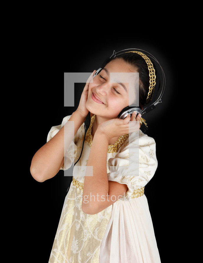 Young girl in ancient dress while listening music with headphones on black background.