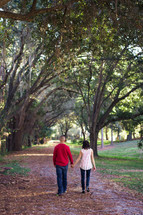 A man and woman holding hands while walking down a path.