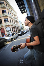 Man playing guitar and singing on sidewalk.