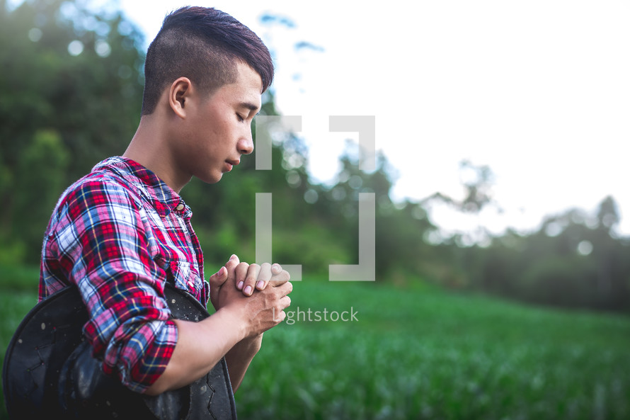 Young farmer sitting praying in a corn field