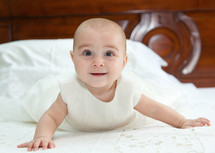 Portrait of a baby in baptismal clothing sitting on bed