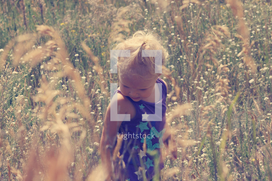 a toddler girl standing in tall grass 