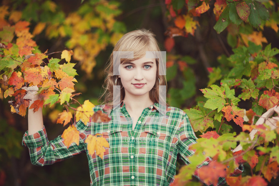 woman holding fall leaves on a tree 