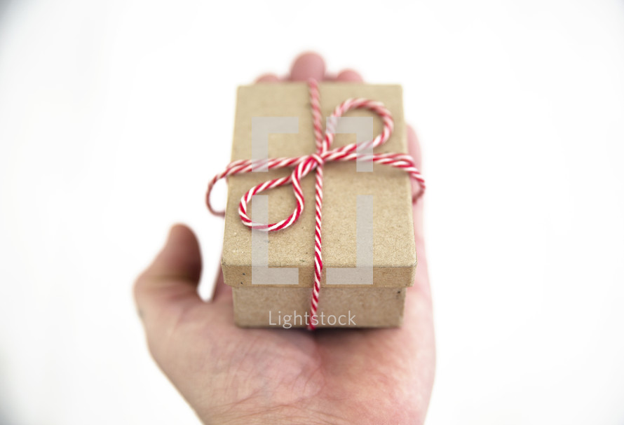 hand holding red and white string around a brown paper gift box 