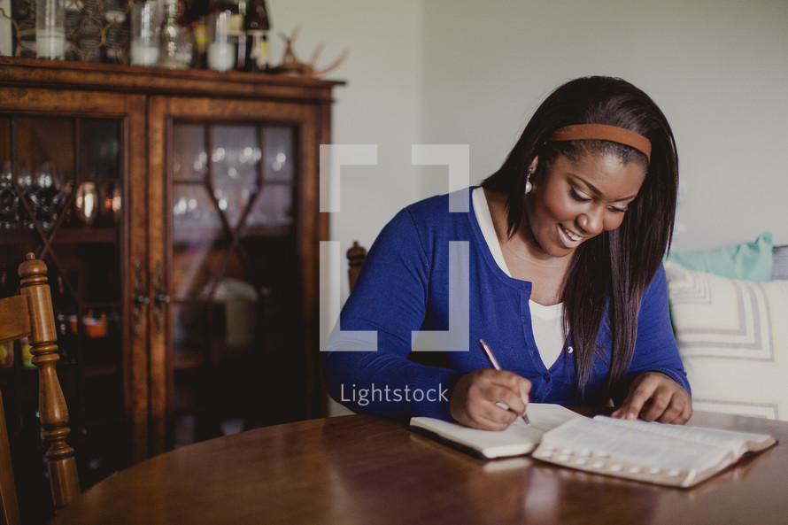 African-American woman reading a Bible and writing in a notebook