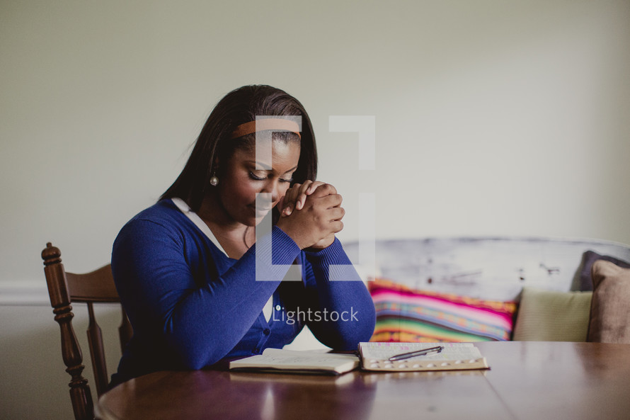 African-American woman praying and reading a Bible and a notebook