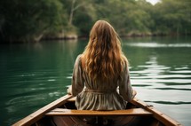 Back view of a woman in a boat on calm water surrounded by trees