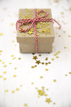 star confetti and red and white string around a brown paper gift box 