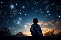 An 8-year-old child sitting under a star-filled sky, gazing upward