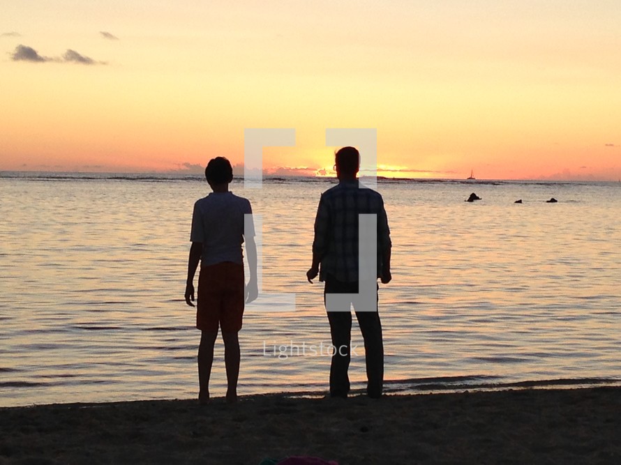silhouette of a man and teenage boy looking out at the ocean 