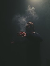 man with outstretched arms standing in smoke in darkness 