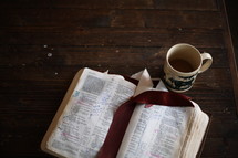 notes on the pages of a Bible and a coffee mug on a table 