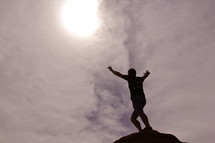 Silhouette of a man with his arms raised on top of a mountain after a hard climb