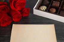 blank paper, box of chocolates, and long stem roses for Valentines day 