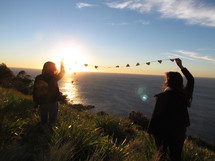 a couple holding a string of paper hearts in the air near the ocean 