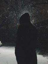 Silhouette of a man standing in the snow at night.