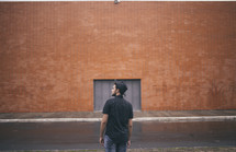 man standing with his back to the camera and a brick warehouse 