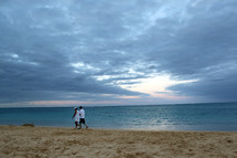 A couple walks along a sandy beach near the water.