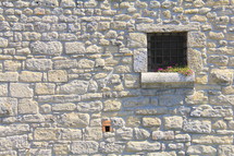 barred window on a castle with flowers growing along the window sill
