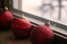 Red Christmas balls sitting on a windowsill.