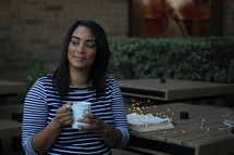 a woman holding a mug and fairy lights on a Bible at an outdoors table 
