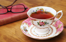 tea in a tea cup, book, reading glasses on a table 