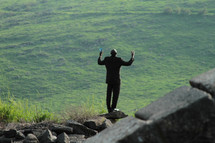 Silhouette of a man in praise and worship on a rock overlooking the ocean.