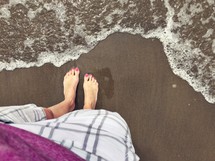 A woman's feet on the edge of the ocean surf.