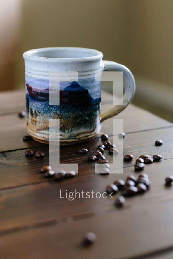 Coffee beans and a coffee cup on a wooden surface.