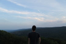 Back of a man standing on a hillside gazing at nature.