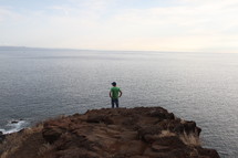 a man standing at the edge of a cliff looking out over the water 