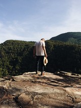 man standing on a rock holding a hat 