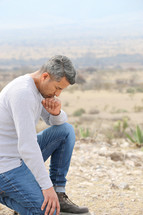 a man kneeling in prayer in a desert