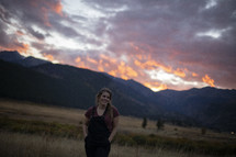 a woman standing in a field at sunset 
