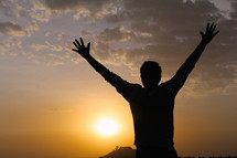Silhouette of a man with raised hands at sunset / sunrise