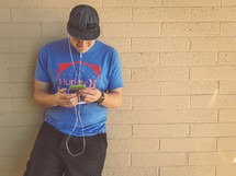 a man listening to earbuds leaning against a wall 